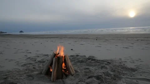 Beach Bonfire with Large Rock in Ocean and Sun Setting Video stock 20485095