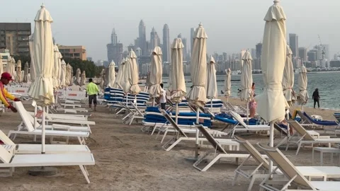 A beach boy stacks sunbeds on Palm Jumeirah's evening shore as golden twiligh Video stock 313388301