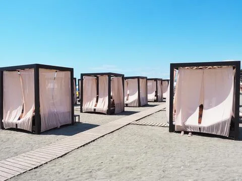 Beach cabins with light curtains stand in a row on the sand with wooden paths Stock Photos