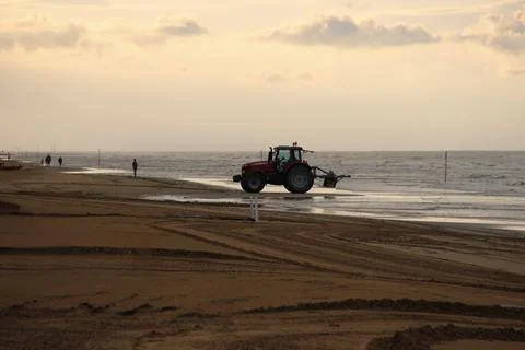 Beach Cleaning Tractor Working on Sandy Shore at Sunset Stock Photos