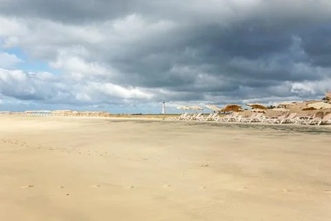 A beach with a cloudy sky and a lighthouse in the distance in Spain canary Stock Photos
