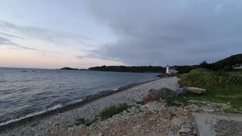 A beach with cobbles during sunset with a lighthouse in the background Stock Footage 161325608