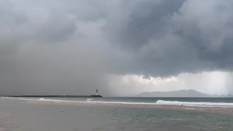 The beach covered in dark clouds, with a lighthouse in the distance Stock Footage 303982180