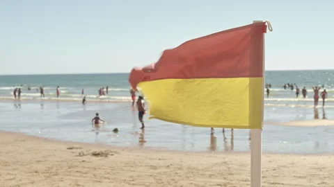 Beach Day With a Flag Flying in the Wind at a Busy Coastline in Summer Stock Footage 344745310