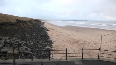 Beach with distant pier and a dark cliff with landslip Stock Footage 260503576