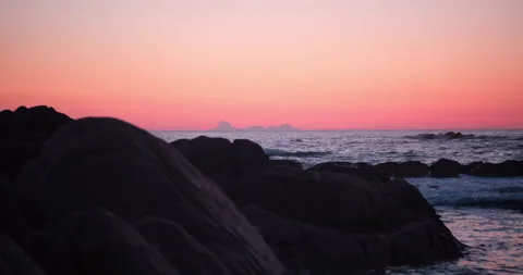 Beach at dusk with red orange gradient sky. Dark rocks in foreground Stock Footage 146175343