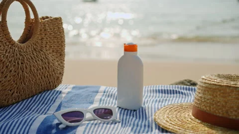 Beach essentials arranged on sandy shore, sunscreen bottle with cap off, UV Stock Footage 270072093