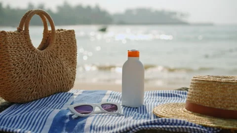 Beach essentials laid out on sandy shore by glistening sea. Striped towel, tote Stock Footage 269047839