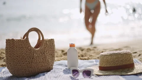 Beach essentials laid on towel, sunscreen bottle, UV protection. Person walks Stock Footage 266813219