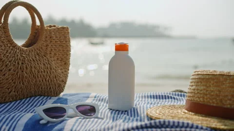 Beach essentials placed on striped towel, white sunscreen bottle, stylish Stock Footage 271301097