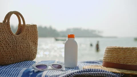 Beach essentials placed on a striped towel near sea during sunny day. Bottle of Stock Footage 271596177