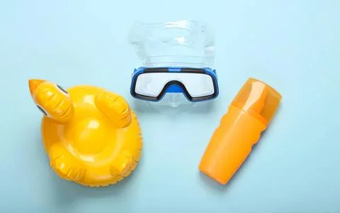 Beach float, goggles, and sunscreen on light blue background Stock Photos