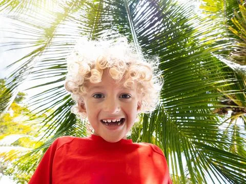 Beach fun. Curly boy under palm tree. Stock Photos
