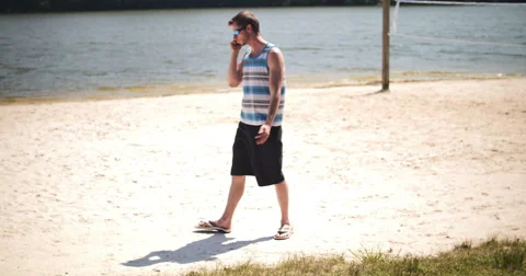 Beach Fun at Lake Young Man Talking on Smart Phone Wide, 4K Stock Footage 64332995