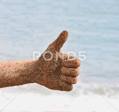 Beach fun with a wet hand with sand on it giving a thumbs up. ocean beach wav Stock Photos