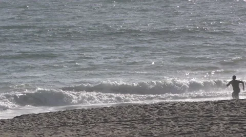 Beach goers runs into the ocean surf while another runs along the shore line. Stock Footage 67618616