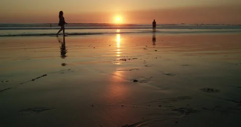 Beach goers walk along beach at sunset 스톡 동영상 138334042