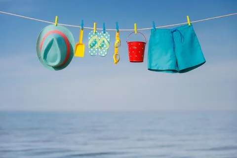 Beach hat, flip-flops and goggles hanging on a clothesline against sea and sk Stock Photos