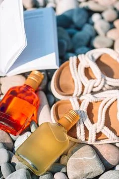 Beach hat on opened book with sunscreen and shoes on pebble beach Stock Photos
