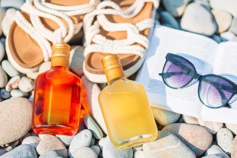 Beach hat on opened book with sunscreen and shoes on pebble beach Stock Photos