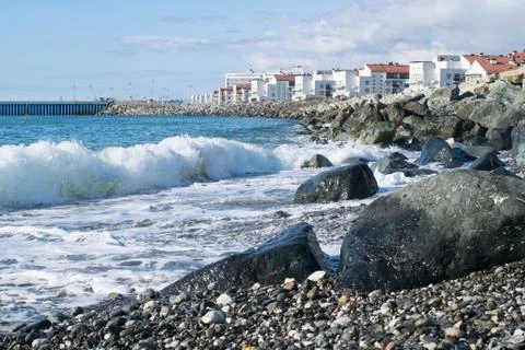 Beach with huge rocks and waves on the background of houses and water area on Stock Photos