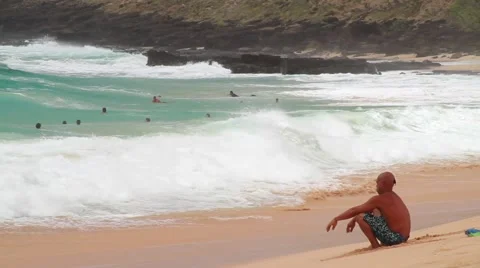 Beach with large waves on a sunny day in Hawaii. Male surfer sits on sand. Video stock 50979567