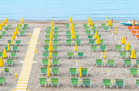 Beach lounge area with yellow umbrellas and green sunbeds on italian coastline. Stock Photos