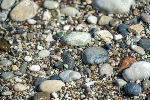 Beach with multicolored small round stones on a sunny day Stock Photos