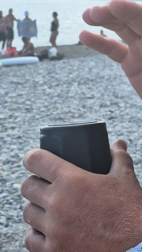 Beach, music, speaker, man tapping portable sound device on pebble shore, people Vidéo 322609547