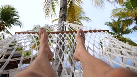 Beach on ocean, hammock is swinging. Close-up: pair of male legs in hammock on Video stock 270483611