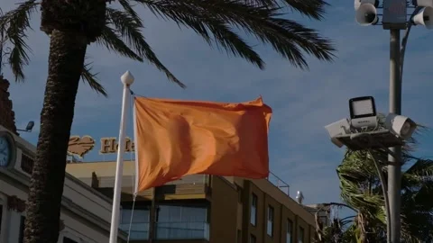 Beach orange level of warning flag on flagstock with palmas and building Stock Footage 166532754