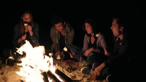 Beach party late at night with bonfire and roasting marsh mellows with friends Stock Footage
