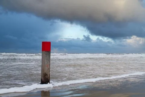 Beach pole with red head at high tide under a dark cloud Stock Photos