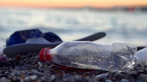 Beach Pollution, Plastic Bottle and other Rubbish on Beach. Person Walking by. Stockbeeldmateriaal 129185656