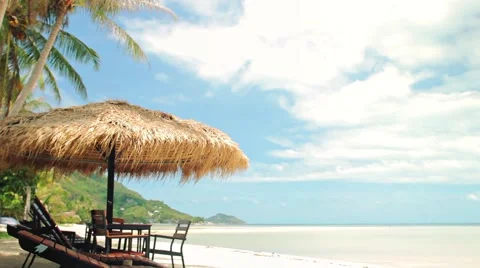 Beach relaxing Sunbeds and a table under straw umbrella at the tropical beach Stock Footage 64291872