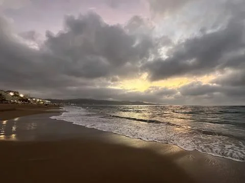 Beach scene with cloudy sky and gentle waves at sunset Stock Photos