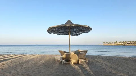 A beach scene in Egypt featuring a straw umbrella and two lounge chairs on the Foto stock