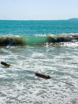 A beach scene shows waves breaking on the shore with a floating object visibl Stock Photos
