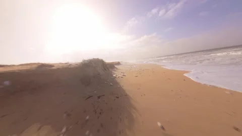 Beach scene with strong sunlight, crashing waves, and wind-blown sand Stock Footage 345058282
