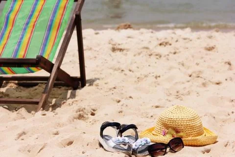 Beach scene. Sun straw hat, sandals and sunglasses lie on the sand on the beach. Stock Photos