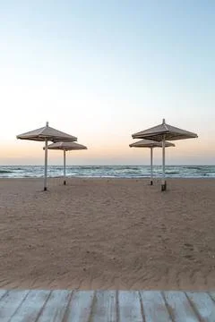 Beach scene with two umbrellas and calm sea at sunset Stock Photos