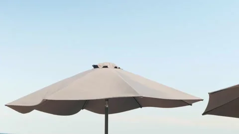 Beach shore, blue sky. Protective beach umbrella from sun. Strong wind Stock Footage 159795046