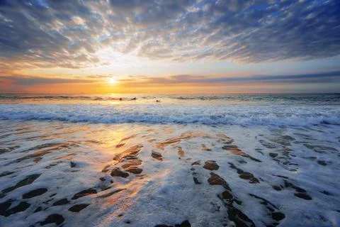 Beach shore at sunset with some surfers Stock Photos