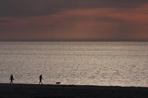 Beach silhouettes at sunset, tranquil evening shoreline Stock Photos