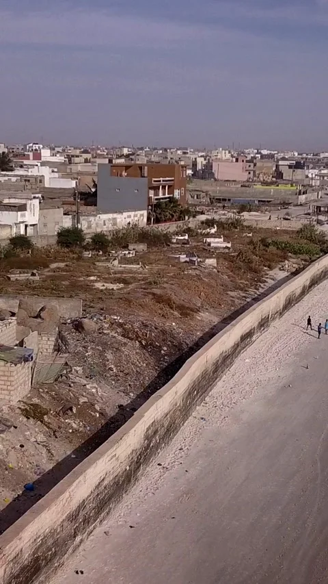 Beach with small wall built along slums, city buildings in background Video stock 230672975