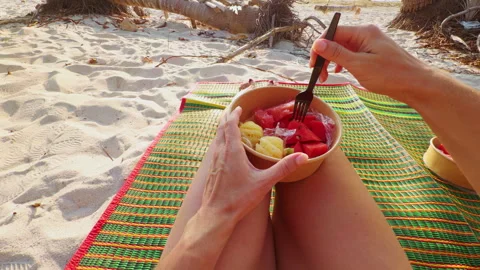 Beach Snack Moment, Hand Holding Watermelon Cube with Fork Above Fruit Bowl on S Stock Footage 332295492