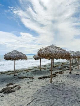 Beach with straw umbrellas and waves in background during cloudy day Stock Photos