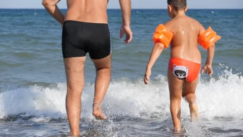 Beach summer vacation. A man and a child run into the raging sea to dive. Stock Footage 119596406