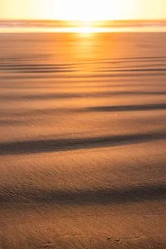 A beach with a sun setting in the background Stock Photos