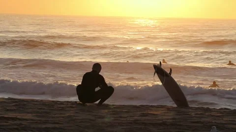 Beach Sunrise with Surfer in foreground while surfers are in the water Stock Footage 235663263